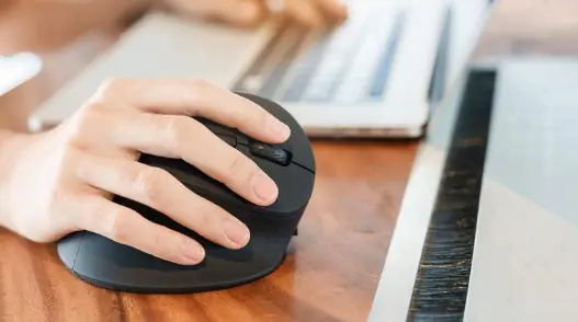 mano sosteniendo mouse ergonómico y otra mano sobre el teclado